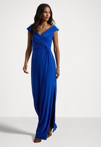 Long blue dress with a fitted bodice, V-neckline, short cap sleeves, and a side slit, made from smooth, stretchy fabric.