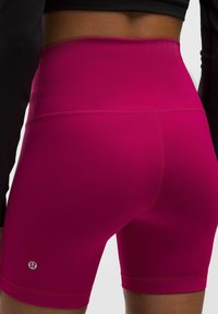Pantalones cortos deportivos de tiro alto en color rosa, hechos de tela elástica con costuras planas y un pequeño logo en la pierna izquierda.