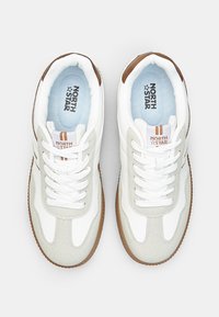 White sneakers with grey suede accents and brown rubber soles. Features classic lacing and a light blue interior with "NORTH STAR" logo.