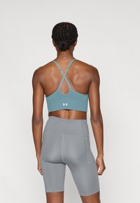 Μπλε αθλητικό σουτιέν με σταυρωτούς ιμάντες, κατασκευασμένο από λείο υλικό, συνδυασμένο με γκρι σορτς ψηλής μέσης με ελάχιστες ραφές.