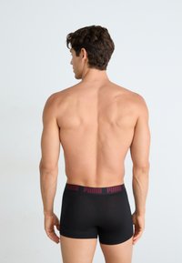 Boxeri scurți negri din bumbac, cu o talie largă ce are inscripția roșie "PUMA". Modelul este prezentat din spate, evidențiind un design ajustat.
