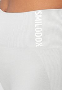 Hellegraue, gerippte Leggings mit einem hohen Bund, auf dem die Marke "SMILODOX" in Weiß vertikal an der Seite gedruckt ist.