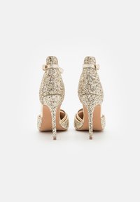 Gold glitter high heel shoes with a pointed toe, featuring a slender stiletto heel and ankle strap. Smooth inner lining and textured exterior.