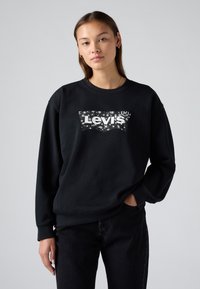 Felpa nera in cotone con collo rotondo, caratterizzata da un logo bianco di Levi's circondato da un motivo di stelle. Abbinata a jeans scuri.