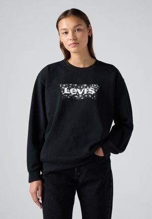 Svart hettegenser laget av bomull med rund hals, preget av en hvit Levi's logo omringet av et stjernesymbol. Kombinert med mørke jeans.