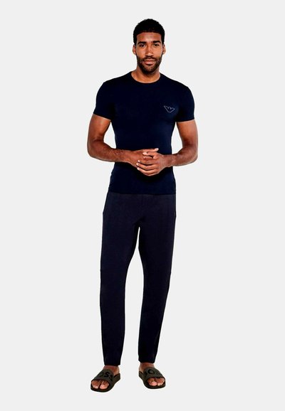 Navy modrý tričko s krátkým rukávem a logem, spárované s tmavými kalhotami a černými šlapkami. Hladká látka, přiléhavý design.