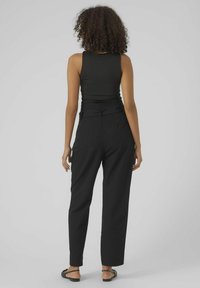 Haut sans manches noir associé à un pantalon noir taille haute et ample. Le pantalon présente un détail de ceinture nouée, une texture lisse et une coupe droite.