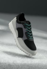 Black and gray sneaker with mesh upper and rubber sole, featuring green laces and a minimalistic design with rounded toe.