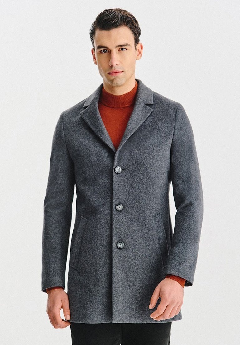 Szary wełniany płaszcz o dopasowanym kroju, z trzema guzikami, kołnierzem z wycięciem i bocznymi kieszeniami, zestawiony z czerwonym golfem pod spodem.