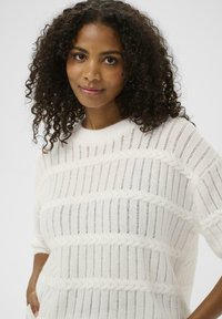 Pull en maille blanche épaisse avec motifs horizontaux, doté d'une coupe ample et de larges manches, confectionné dans un fil doux et texturé.
