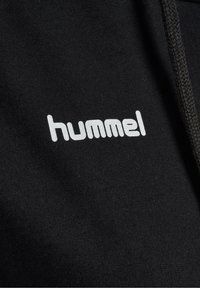 Tissu noir avec texte de marque « hummel » blanc imprimé, gros plan montrant une partie d'un cordon texturé sur le côté droit.