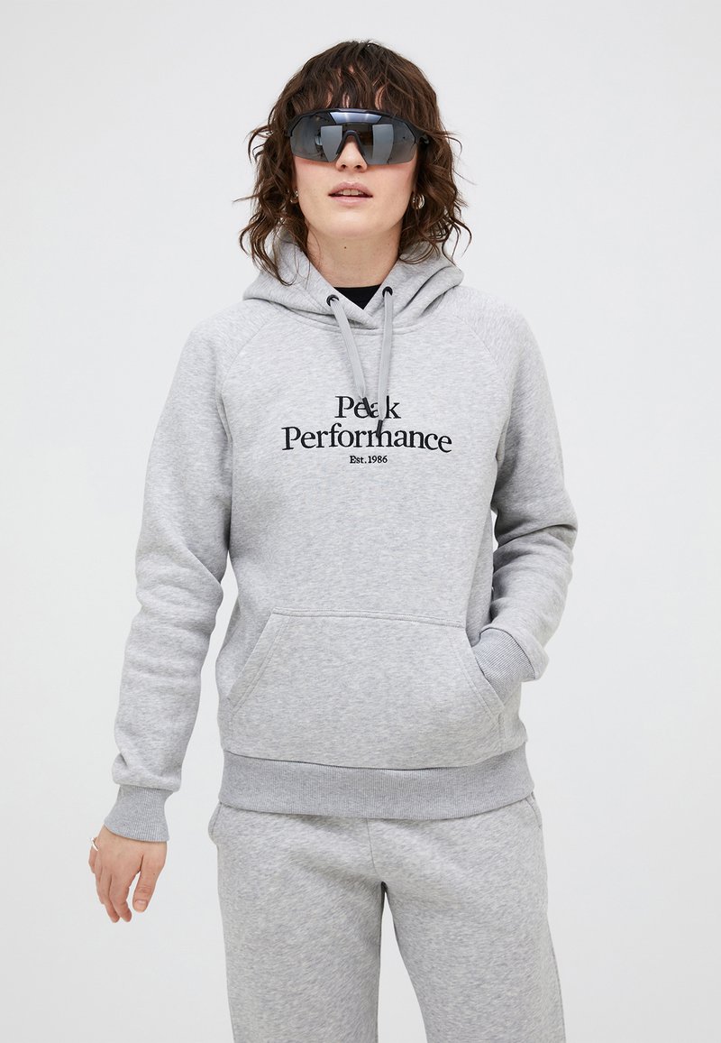 Grå hættetrøje med frontlomme og trykt tekst "Peak Performance Est. 1986" i sort. Blødt tekstureret stof, afslappet pasform.
