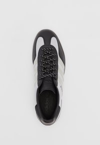 Black and white athletic shoe with a textured mesh upper, black leather accents, three white stripes, and black laces with silver threading.
