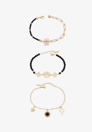 Tre braccialetti in tono oro: uno con perline nere e un ciondolo quadrato rosa, uno con perline nere e motivi floreali traforati, uno con ciondoli a stella, rotondi e a croce.