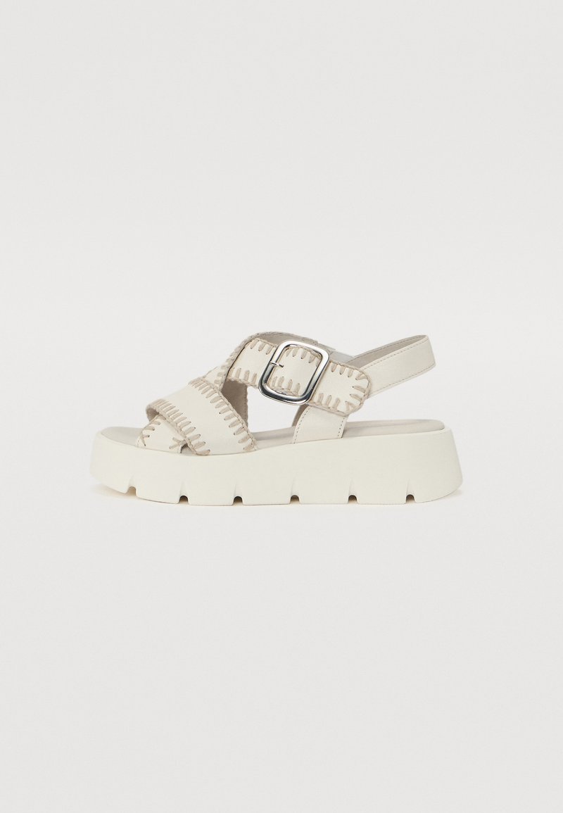 Beige plattform sandaler med kryssremmer og spenne. Har teksturert søm og en kraftig hvit såle. Glatt lærmateriale.