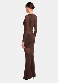 Braunes langärmeliges Kleid mit tailliertem Oberteil und schwingendem Saum. Hergestellt aus einem glatten Stoff, der transparente Einsätze an den Seiten aufweist.