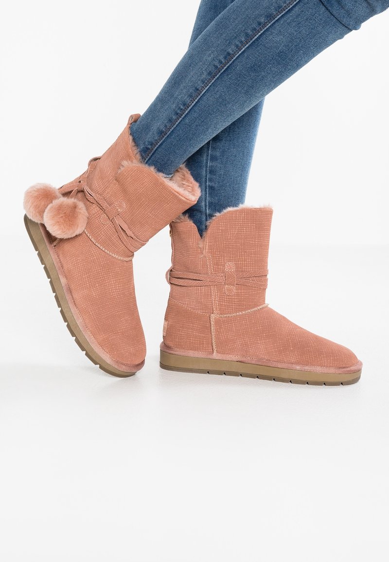 Růžové semišové kotníkové boty s umělou kožešinou, strukturální povrch a plochou gumovou podrážkou. Mají detaily se stuhou po straně a otevřený vršek.