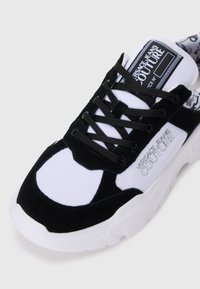 Svart og hvit sneakers som har en blanding av semsket skinn og syntetiske materialer, rund tå, tykk såle, flate lisser og fremtredende logo-detail.