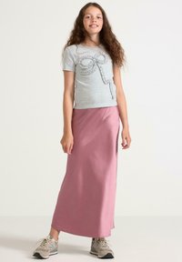 T-shirt grigio chiaro a maniche corte con dettagli a ruches a forma di fiocco, abbinato a una gonna lunga in satin rosa e sneakers beige.