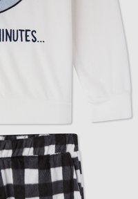 Maglione bianco in pile a maniche lunghe con stampa e testo blu, abbinato a pantaloni da pigiama in peluche a quadri bianco e nero.