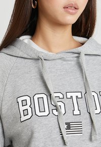 Szara bluza z kapturem z troczkami, ozdobiona wyraźnym napisem "BOSTON" oraz wzorem amerykańskiej flagi. Miękki materiał, luźny krój, z efektem warstwowym.