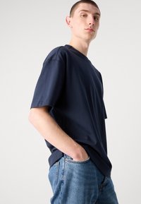 Námořnická modrá bavlněná tričko s volným střihem, krátkými rukávy a kulatým výstřihem. V kombinaci s světle modrými džínovými kalhotami.