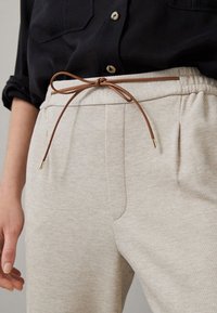 Hellgraue, strukturierte Sweatpants mit einem Kordelzugbund. Ausgestattet mit einem braunen Kordelzug mit Metallenden und seitlichen Taschen.