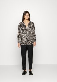 Camisa em padrão leopardo nas cores bege e preto, com decote em V e mangas longas, combinada com calças pretas ajustadas e sapatos pretos.