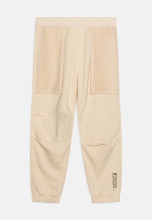 Beige joggebukser i blødt stof med elastisk talje, der har to mesh-lommer foran og et logo-detail på underbenet.