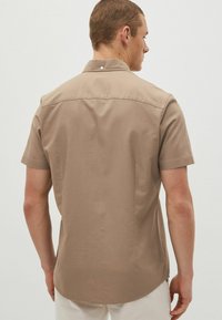 Camicetta a maniche corte beige, con bottoni, realizzata in cotone, dal taglio dritto, con colletto standard e un bottone singolo sul retro.