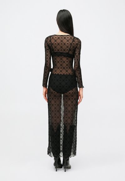 Čierne priesvitné čipkované šaty s dlhými rukávmi, s kvetinovým vzorom a bočnými rozparkami, nosené cez čierne šortky s vysokým pásom a členkové topánky.