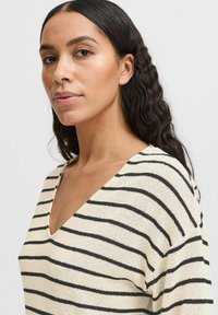 Gestreifter Strickpullover in Creme mit schwarzen horizontalen Streifen, mit tiefem V-Ausschnitt und weicher Textur. Schlichtes, lässiges Design.