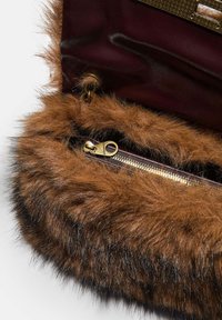 Interno di una borsa in finta pelliccia marrone con una tasca a zip dorata, foderato di un profondo bordeaux e con dettagli in pelle testurizzata.