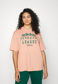 Rožinė trumpomis rankovėmis marškinėliai, su žaliais "adidas ATHLETIC LEAGUE" užrašais, pagaminti iš medvilnės, su laisvu siluetu ir apvaliu kaklu.