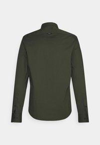 Camisa de manga larga color verde oliva con cuello clásico, puños abotonados y una textura suave. Presenta un dobladillo curvado y una pequeña etiqueta en el cuello.