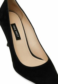 Décolleté nera in suede con punta affusolata, presenta un interno beige liscio e un tacco basso e sottile. Etichetta del marchio visibile all'interno.