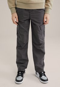 Cargo-Hose aus dunkelgrauem Stoff, mit Seitentaschen und lockerer Passform. Trägt man mit schwarz-grauen Sneakers für einen lässigen Look.