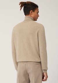 Maglione a collo alto beige in maglia, con maniche lunghe, polsini e orlo rigati. Texture morbida, silhouette aderente e design minimalista.