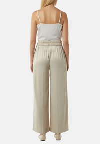 Brede beige broek met een elastische tailleband, gecombineerd met een wit mouwloos topje met dunne banden en een gladde textuur.