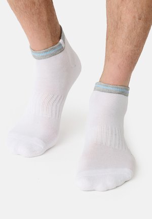 Feet wearing white ankle socks with gray and light blue trim, standing on a white surface.