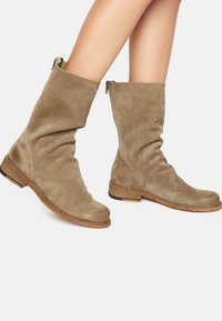 Bottes en suède taupe, avec un design flou, bout rond et semelle en bois épaisse avec un accent noir. Fermeture éclair à l'arrière.