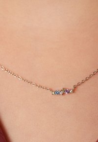 Zilveren ketting met een cluster van vier edelstenen: geel, blauw, lichtpaars en donkerpaars, gezet in ronde instellingen.
