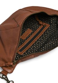 Intérieur d'un sac en cuir marron avec un tissu noir à pois dorés, un poche zippée et une étiquette de marque. Coutures piquées le long des bords.