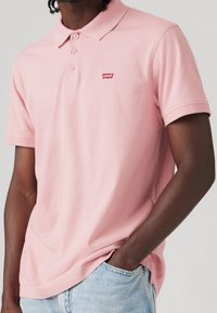Polo en coton rose avec col classique, patte de boutonnage à trois boutons et petit logo rouge Levi's sur la poitrine gauche. Porté avec un jean clair.