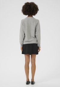 Gray knit sweater with long sleeves and ribbed hem, paired with a black A-line skirt. Legs visible, wearing black shoes with silver studs.