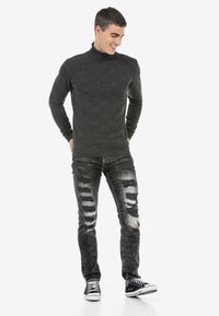 Schwarzer Rollkragenpullover mit strukturiertem Muster, kombiniert mit ausgewaschenen schwarzen Jeans. Sneakers mit weißen Sohlen runden das Outfit ab.