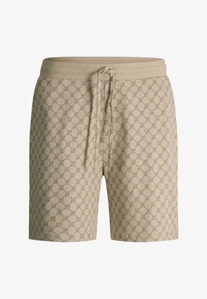 Pantalones beige con cordón y un patrón geométrico repetido en gris oscuro, usados con una camisa blanca metida por dentro.