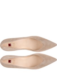 Ballerines en daim beige à bout pointu avec un décolleté bas, présentant un petit accent rouge près du talon et des semelles intérieures lisses beige.