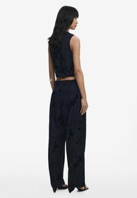 Woman wearing navy blue sleeveless cropped top and wide-leg pants with subtle floral print, standing sideways on white background.