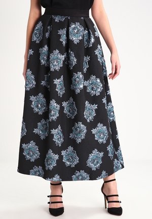 Mujer con falda midi negra con estampados florales azules y plateados y zapatos de tacón negro con tiras en el tobillo.